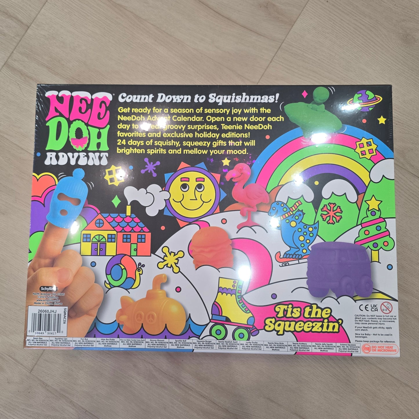 A colorful Nee Doh Advent toy box photographed on a light wood floor. The packaging features bright cartoon graphics including a rainbow, smiley face, stars, and a hand squeezing a blue object, with the text 'Nee Doh Advent' and 'It's the Squezzin'.
