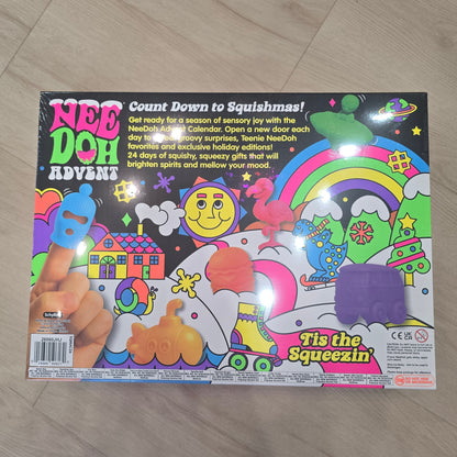 A colorful Nee Doh Advent toy box photographed on a light wood floor. The packaging features bright cartoon graphics including a rainbow, smiley face, stars, and a hand squeezing a blue object, with the text 'Nee Doh Advent' and 'It's the Squezzin'.